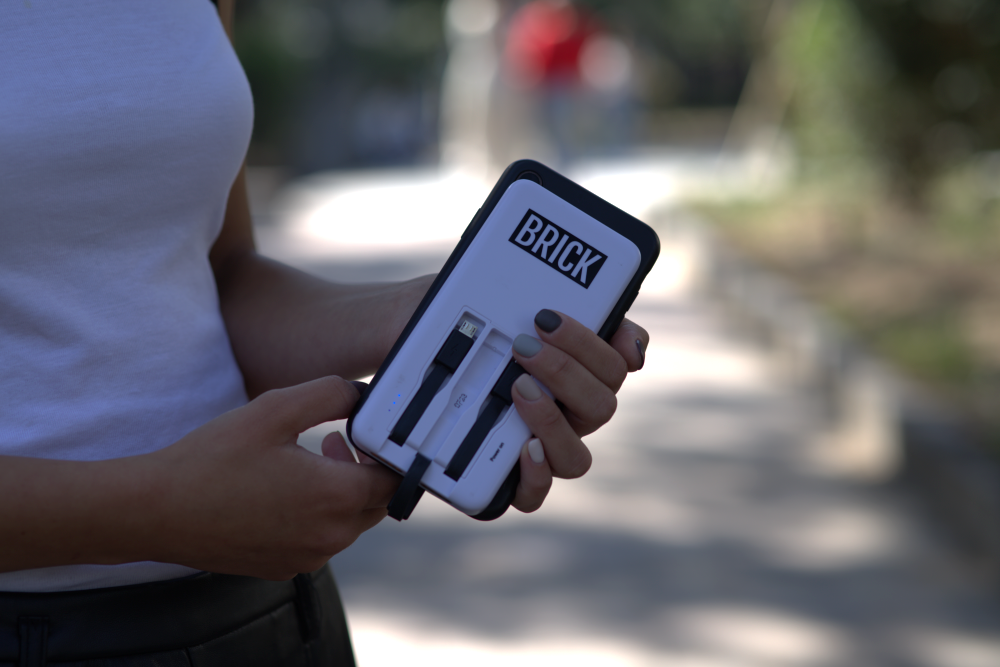 Picture of a person holding their phone, with the Brick powerbank.