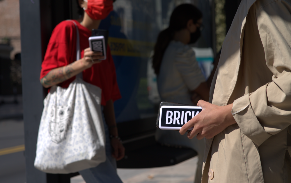 Two persons waiting on the bus or train, both holding a powerbank in their hand.