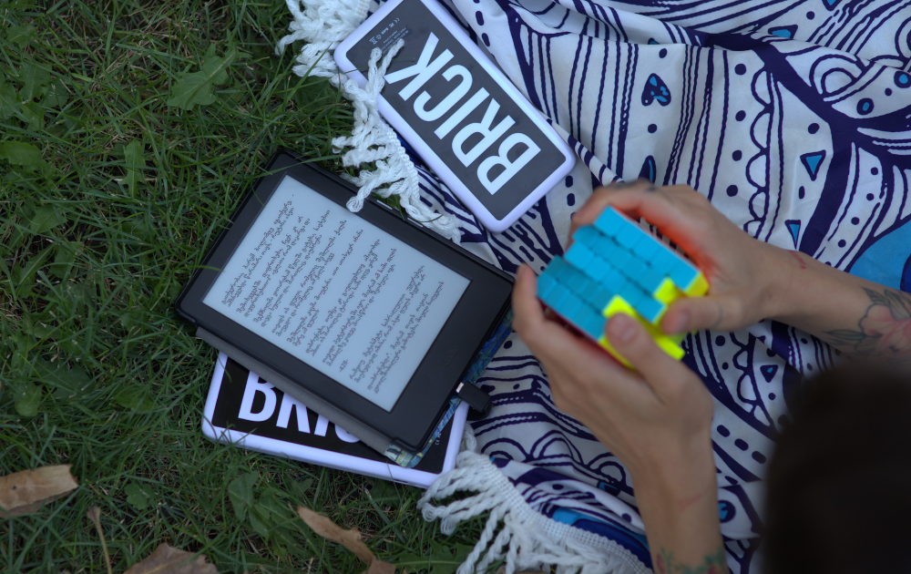 A picture of a person sitting on a lawn, while charging their tablet with a Brick powerbank.